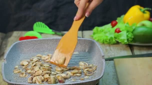 Una mano femenina con una espátula revuelve champiñones fritos en una sartén — Vídeos de Stock