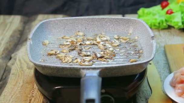 De vrouwelijke hand schuift de kip over in een pan met gebakken champignons — Stockvideo