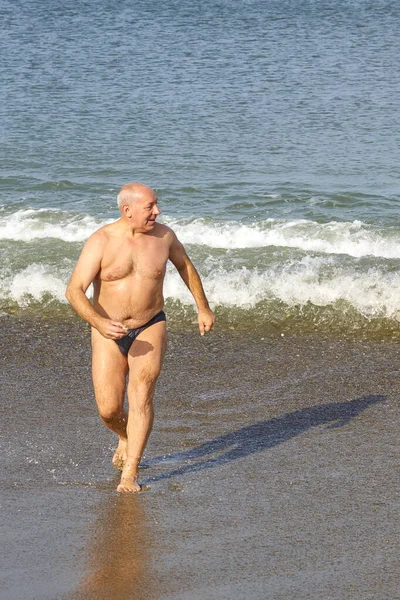 Denizden kumlu sahile koşan bir adam.