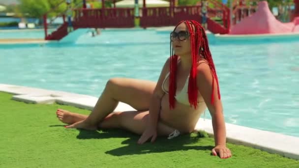 En ung brunett kvinna i en baddräkt sunbathes vid poolen — Stockvideo