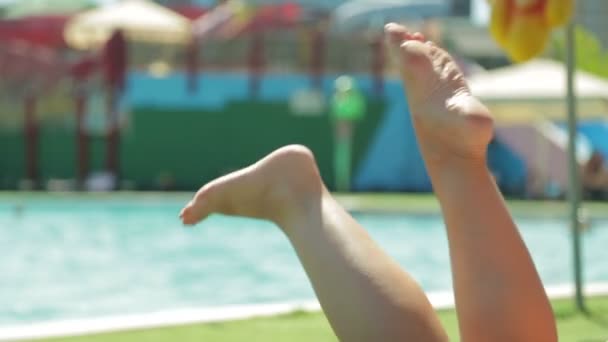 Pernas femininas em uma cadeira de praia junto à piscina . — Vídeo de Stock