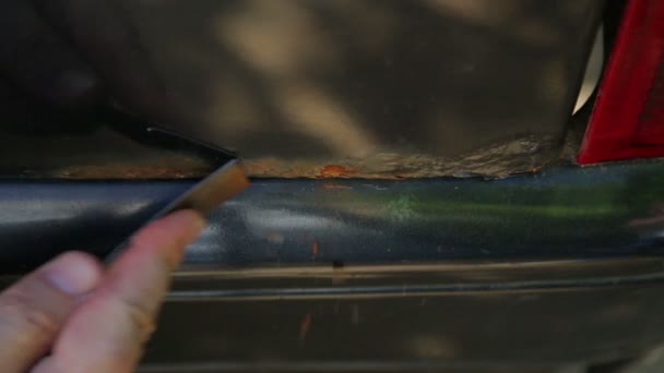Egy ember megtisztítja a rozsda egy autó test egy kaparó — Stock videók