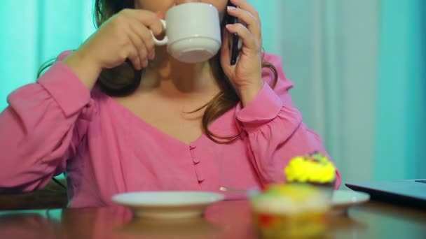 Рыжая женщина за столом в кафе, пьет кофе и разговаривает по телефону . — стоковое видео