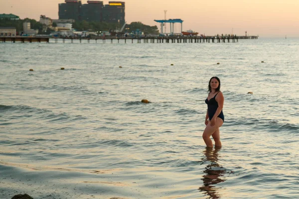 Una mujer en traje de baño azul camina por la orilla del mar al atardecer . — Foto de Stock