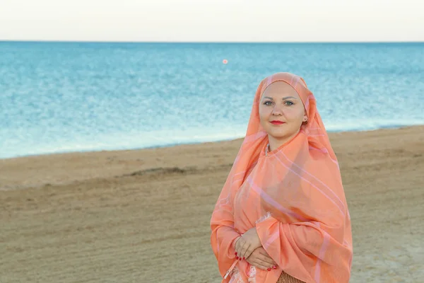 Una mujer musulmana en una bufanda naranja está en la orilla del mar . — Foto de Stock