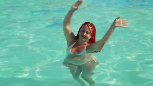 Gelooide vrouw met staartjes dansend in het zwembad met opgeheven handen — Stockvideo