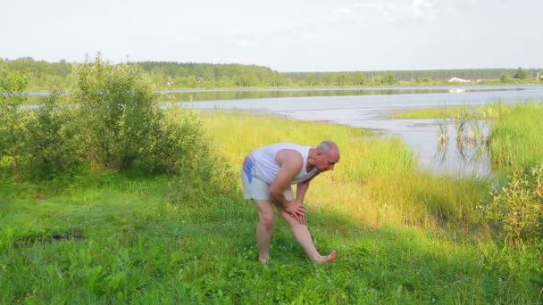 A middle-aged man exercises on the lake in the morning — Stock Video