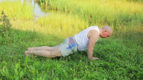 Een man van middelbare leeftijd doet push-ups op het meer in de ochtend — Stockvideo