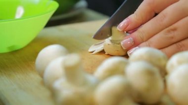 Dişi el, tahta bir tahtanın üzerinde şampiyon mantarları dilimliyor..