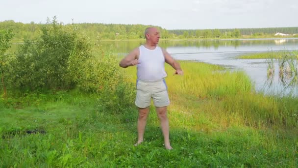 En medelålders man gör yoga på andningsövningar på sjön på morgonen — Stockvideo