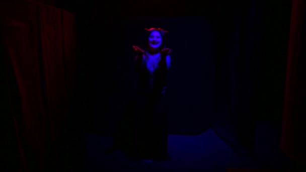 Kobieta w diabelskim kostiumie ze złowieszczym uśmiechem tańczy w czerwonym świetle na czarnym tle — Wideo stockowe