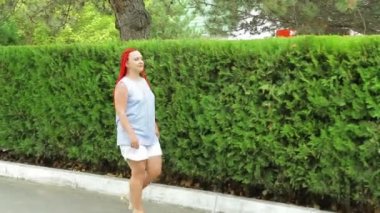 Kızıl saçlı bir kadın yeşil alanlar boyunca yürüyor.