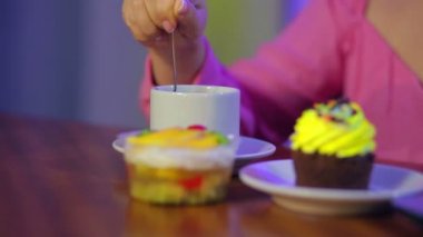 Bir kadın eli kahveye karışıyor. Masada keklerle birlikte.