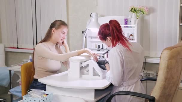 Женщина-маникюрша в перчатках в салоне красоты режет кутикулу на ногтях клиента — стоковое видео