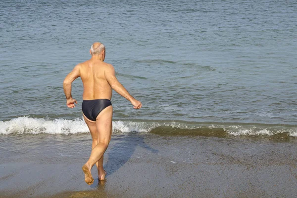 Een man met een run komt de zee binnen vanaf de zandkust.. — Stockfoto
