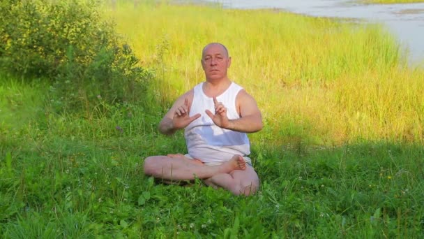Um homem de meia idade faz ioga respiração e medita no lago pela manhã — Vídeo de Stock