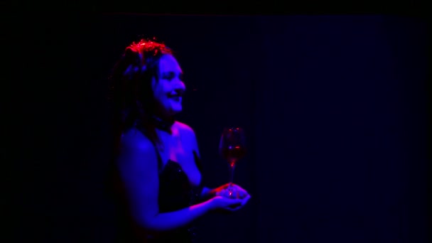 En kvinnlig djävul med ett illavarslande leende på läpparna håller fram ett glas blod för att försegla ett avtal — Stockvideo