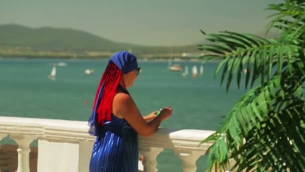 Une jeune femme mange de la glace sur la promenade et regarde la mer . — Video