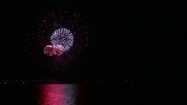 Искрящийся цветовой праздничный фейерверк в ночном небе над рекой, отражающийся в воде — стоковое видео
