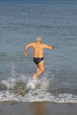 Koşan bir adam kumlu bir sahilde denizlere giriyor..