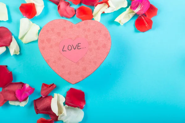 Hart van rozenblaadjes op een blauwe achtergrond en een hartvormige doos met een geschenk en handtekening Love. — Stockfoto