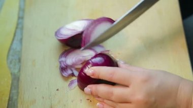 Kadın eli, kırmızı soğanı tahta bir tahtanın üzerinde bıçakla kesiyor.