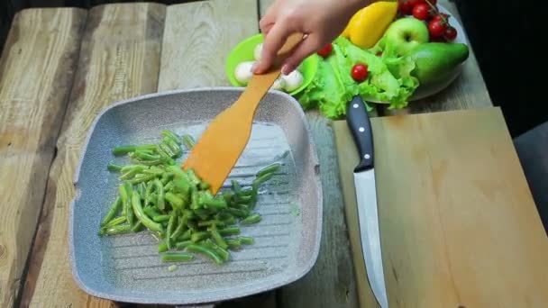 Vrouwelijke hand met een houten spatel roert groene bonen gebakken in olie in een pan — Stockvideo