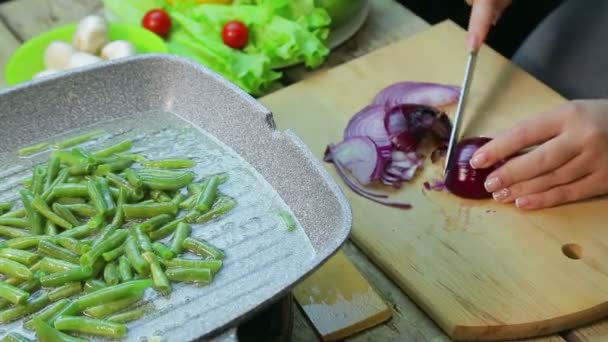 A woman puts chopped onions in a pan with green beans — ストック動画