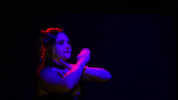 En kvinna i djävulsdräkt med ett illavarslande leende skriker i rött ljus på en svart bakgrund — Stockvideo