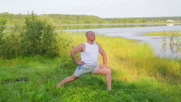 En medelålders man gör stretchingövningar på sjön på morgonen — Stockvideo