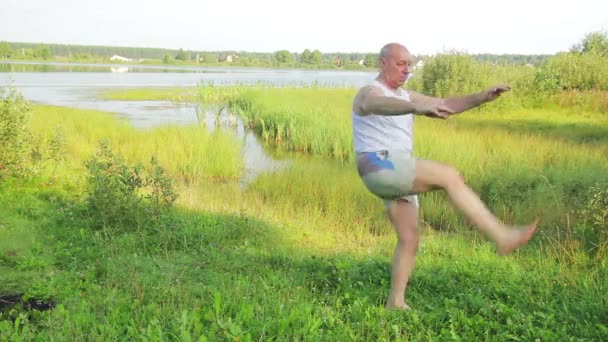 Starszy mężczyzna robi ćwiczenia rozciągające nad jeziorem w godzinach porannych — Wideo stockowe