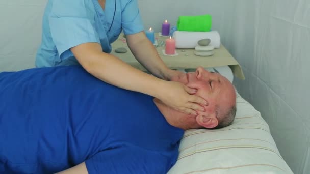 Женщина косметолог делает клиенту мужской массаж лица в спа-салоне — стоковое видео
