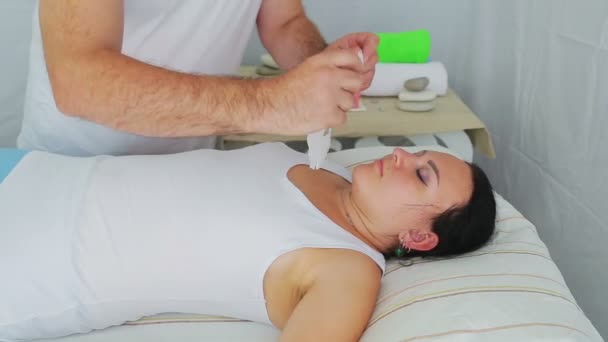 Um cosmetologista masculino aplica uma máscara facial hidratante a uma cliente mulher em um salão de spa — Vídeo de Stock