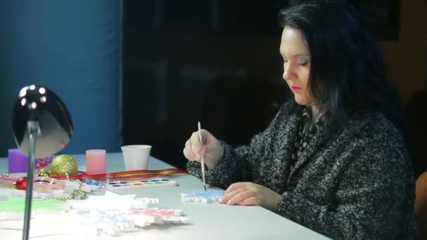 W zimowy wieczór młoda kobieta robi dekoracje świąteczne malując płatki śniegu niebieskim akwarelą — Wideo stockowe
