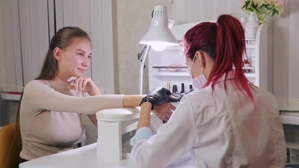 Женщина-маникюрша в перчатках в салоне красоты делает клиенту аппаратный маникюр перед нанесением гелевого покрытия — стоковое видео