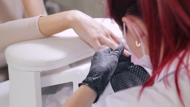 Γυναίκα μανικιουρίστα με γάντια σε ένα σαλόνι ομορφιάς κάνει ένα μανικιούρ υλικού σε έναν πελάτη πριν από την εφαρμογή μιας επίστρωσης τζελ. — Αρχείο Βίντεο