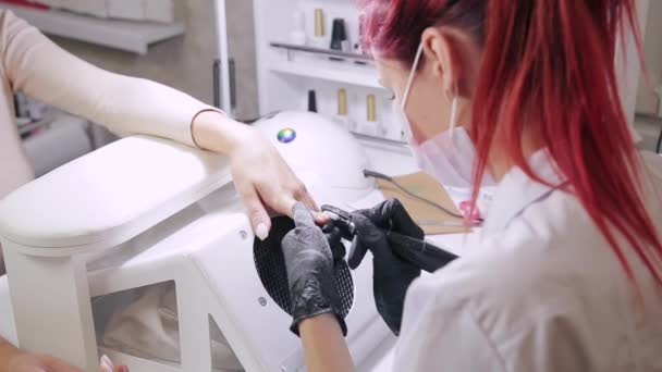 Un manucure dans des gants polit les ongles d'un client avec un appareil avant d'appliquer des revêtements de gel dans un salon de beauté — Video