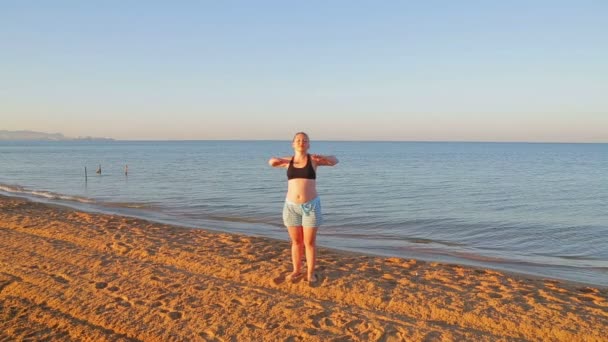 Une femme brune en short fait des exercices d'étirement sur le bord de la mer — Video