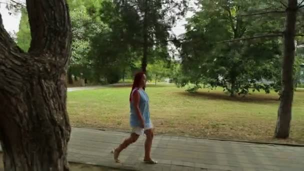 En kvinna går längs en stengångväg i en park. — Stockvideo
