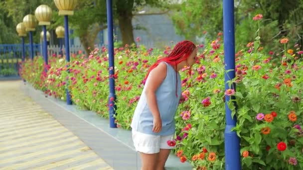 Žena s červenými vlasy obdivuje krásné květiny v parku. — Stock video