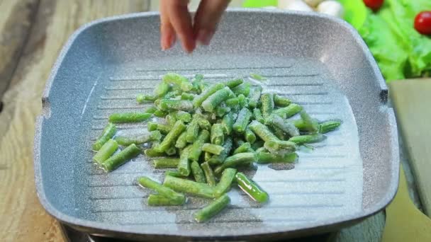 Une main de femme pose des haricots verts sur une poêle chaude . — Video