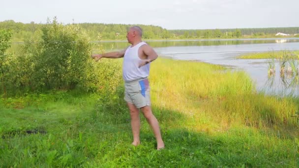 Åldrad man gör stretchingövningar på sjön på morgonen — Stockvideo