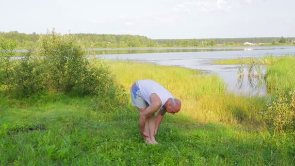 Ein Mann mittleren Alters, der sich morgens an den Hängen am See körperlich betätigt — Stockvideo
