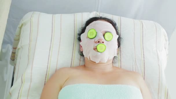 Un estetista maschio mette cetrioli freschi nel salone spa sul viso dei clienti — Video Stock