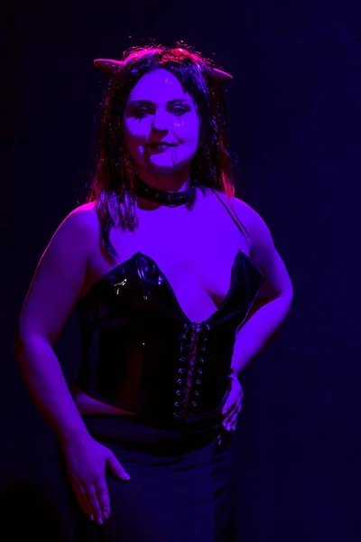 Женщина в облике дьявола на черном фоне в фиолетовом свете улыбается . — стоковое фото