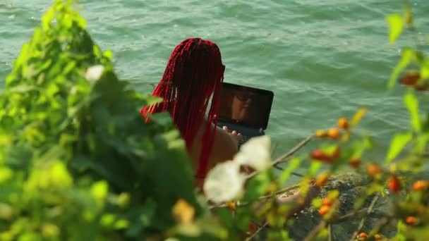 Una mujer con el pelo rojo está blogueando en la orilla contra el telón de fondo de las montañas . — Vídeo de stock