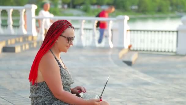 Young tanned woman freelancer working with a laptop on the promenade. — Stock Video