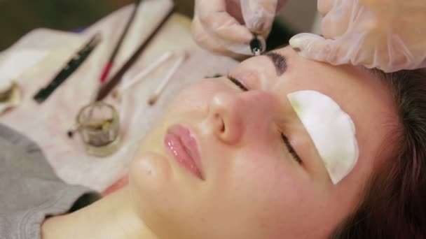 Den kosmetolog tvättar Henna från klientens ögonbryn och applicerar en speciell kräm — Stockvideo