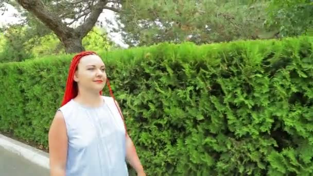 Uma mulher com cabelo vermelho caminha ao longo dos espaços verdes — Vídeo de Stock