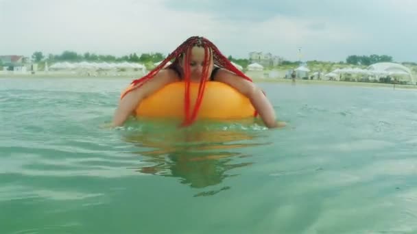 Een jonge vrouw zwemt in de zee in een zwemcirkel. — Stockvideo
